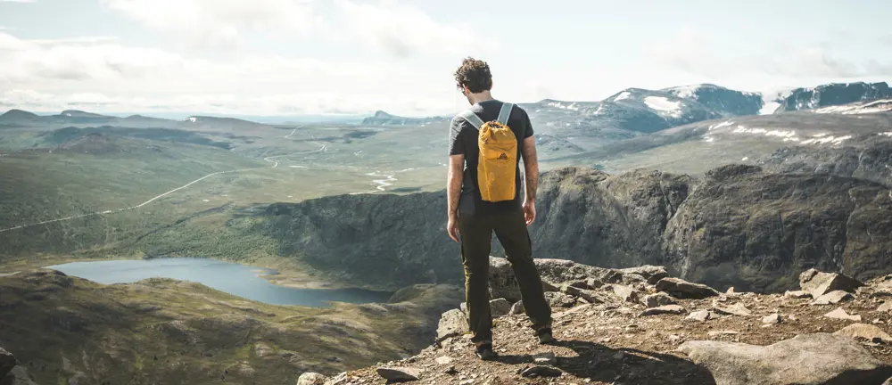 Mann med gul sekk som står på en fjellkant