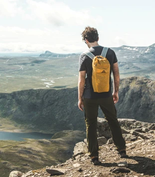 Mann med gul sekk som står på en fjellkant