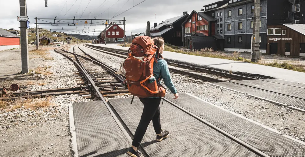 Person med ryggsekk som går over toglinjer.