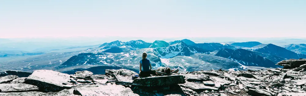 To personer som ligger på en stein og ser utover et fjellområde