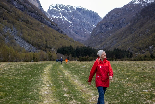 En dame i rød jakke som går tur inne i en dal.