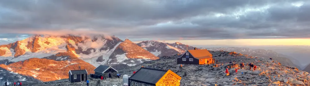 Solnedgang og liv på Fannaråkhytta. Hurrungane sees i bakgrunnen, mens Lusterfjorden kan skimtes til høyre.  [vegard.r.stenerud@gmail.com, 48007757] DNTs Fotokonkurranse- DNT hytteliv. Vår 20123. plass
