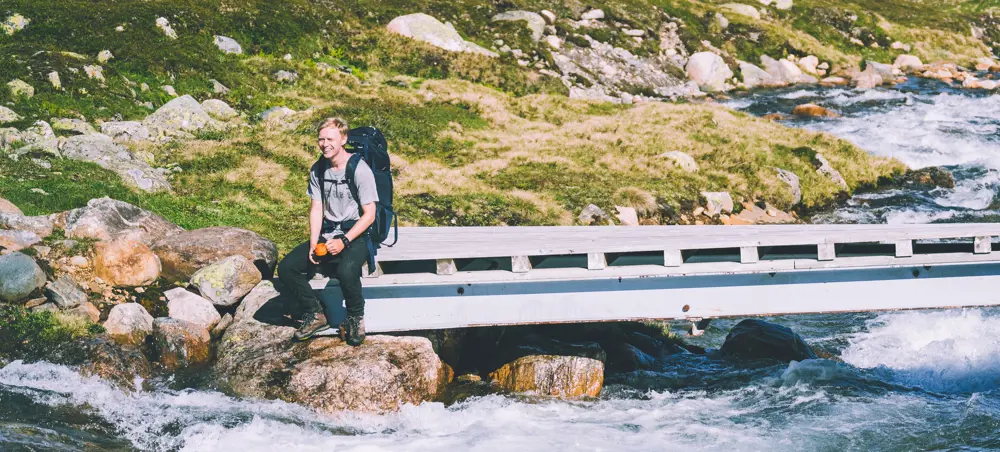 En person som sitter på en bro ved en elv i fjellet