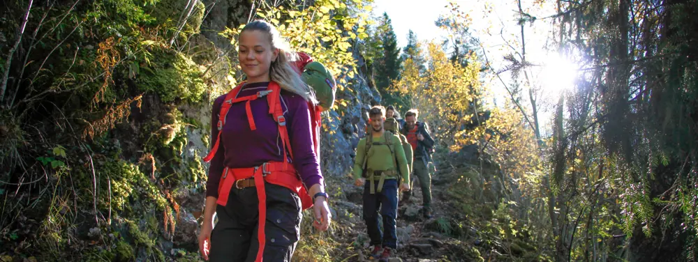 Personer med sekk som går på en sti i skogen