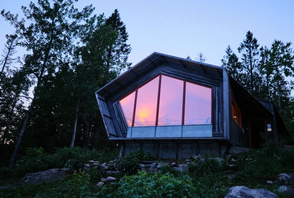 En hytte med store glassvinduer og solnedgang som reflekteres i vinduene