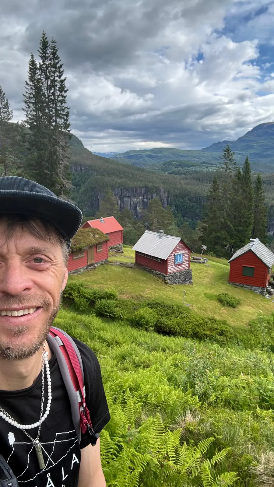 Smilende mann med caps og t-skjorte står foran rødmalt stølstun.