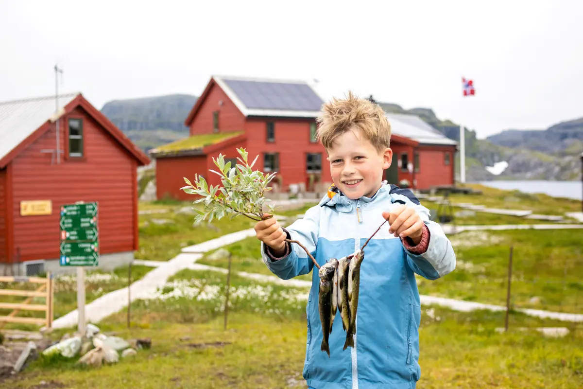 En gutt viser fram tre fisk som er festet på en kvist.