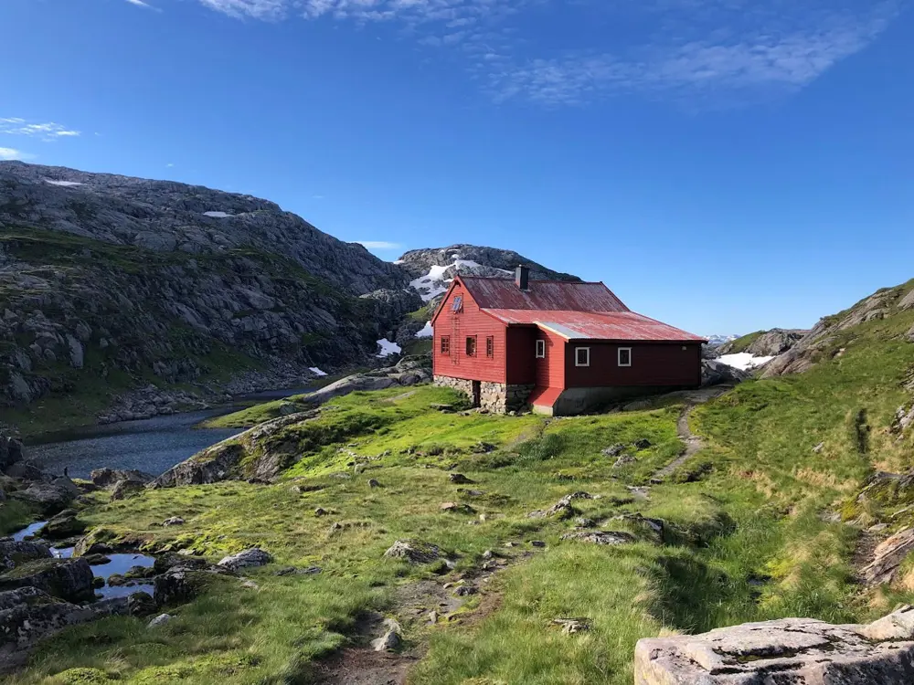 Rødmalt hytte med slitt tak omkranset av fjell.