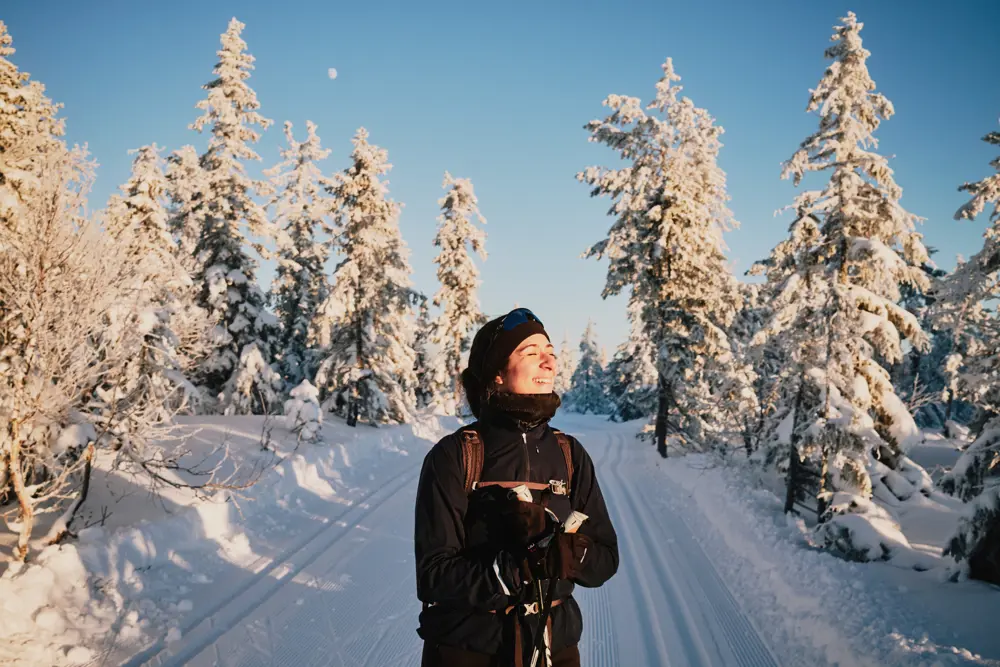 Smilende kvinne på ski i snødekt skog. 