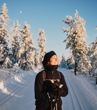 Smilende kvinne på ski i snødekt skog.