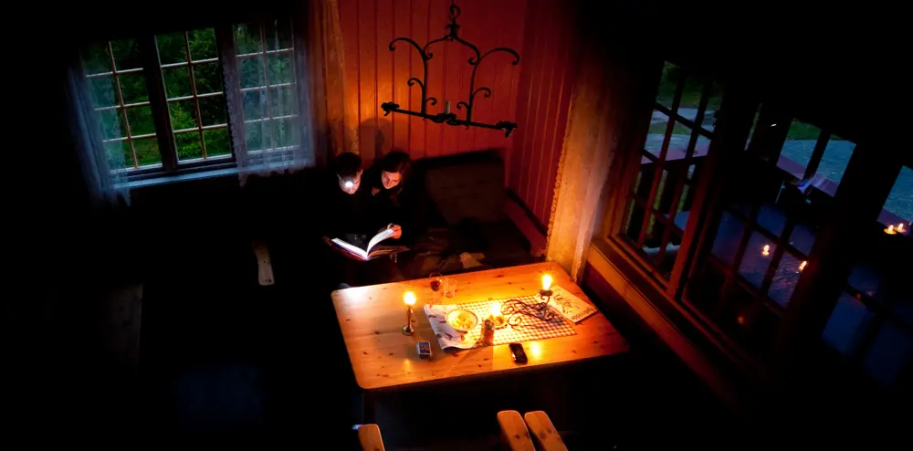 To personer som sitter ved et bord med levende lys og hodelykt og leser. 