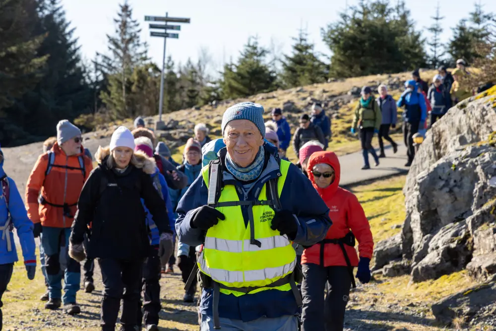 Senior turleder på tur i gul refleksvest med flere turgåere bak seg.