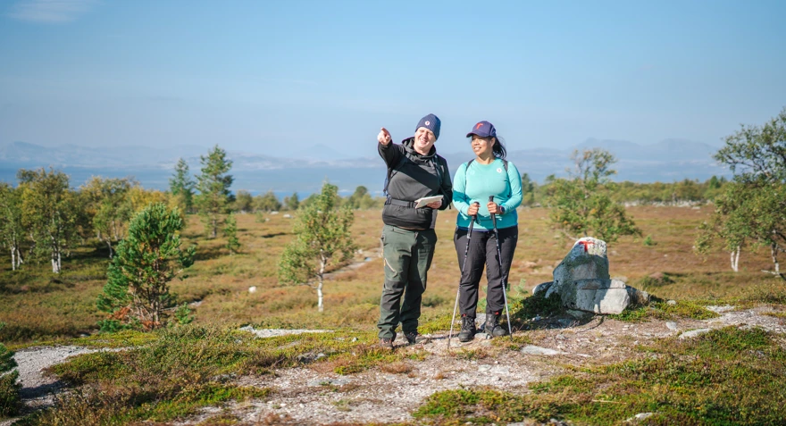 To personer som ser dit mannen peker. De står i et fjellområde, det er blå himmel