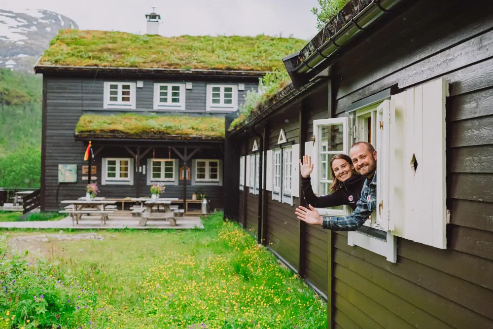 Bilde av to personer som vinker fra vinduet i hytta.